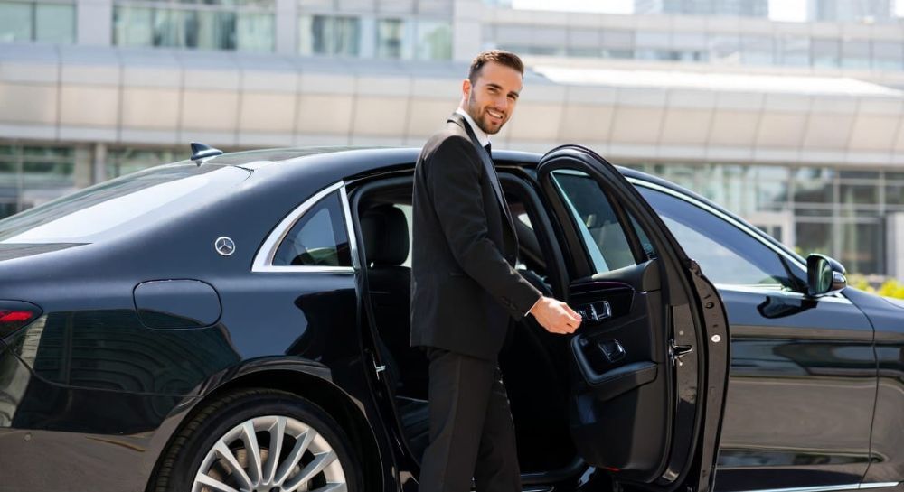 Professional chaueur in a dark suit opening the rear door of a black luxury sedan in Toronto