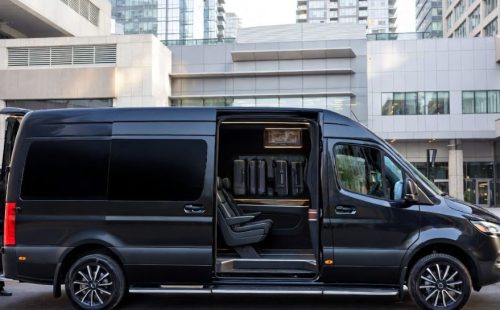 Black Mercedes-Benz Sprinter executive van with open sliding and rear doors, chauffeur in uniform standing at the back.
