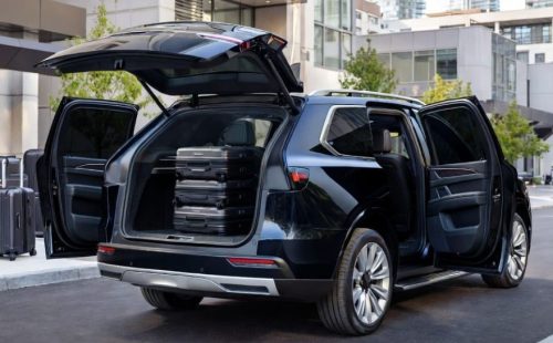 Black luxury SUV with all doors and trunk open, showing spacious interior and stacked hardside suitcases in the boot.