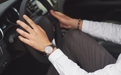 A businessman rides his car, moves on the wheel. Hand with watch.
